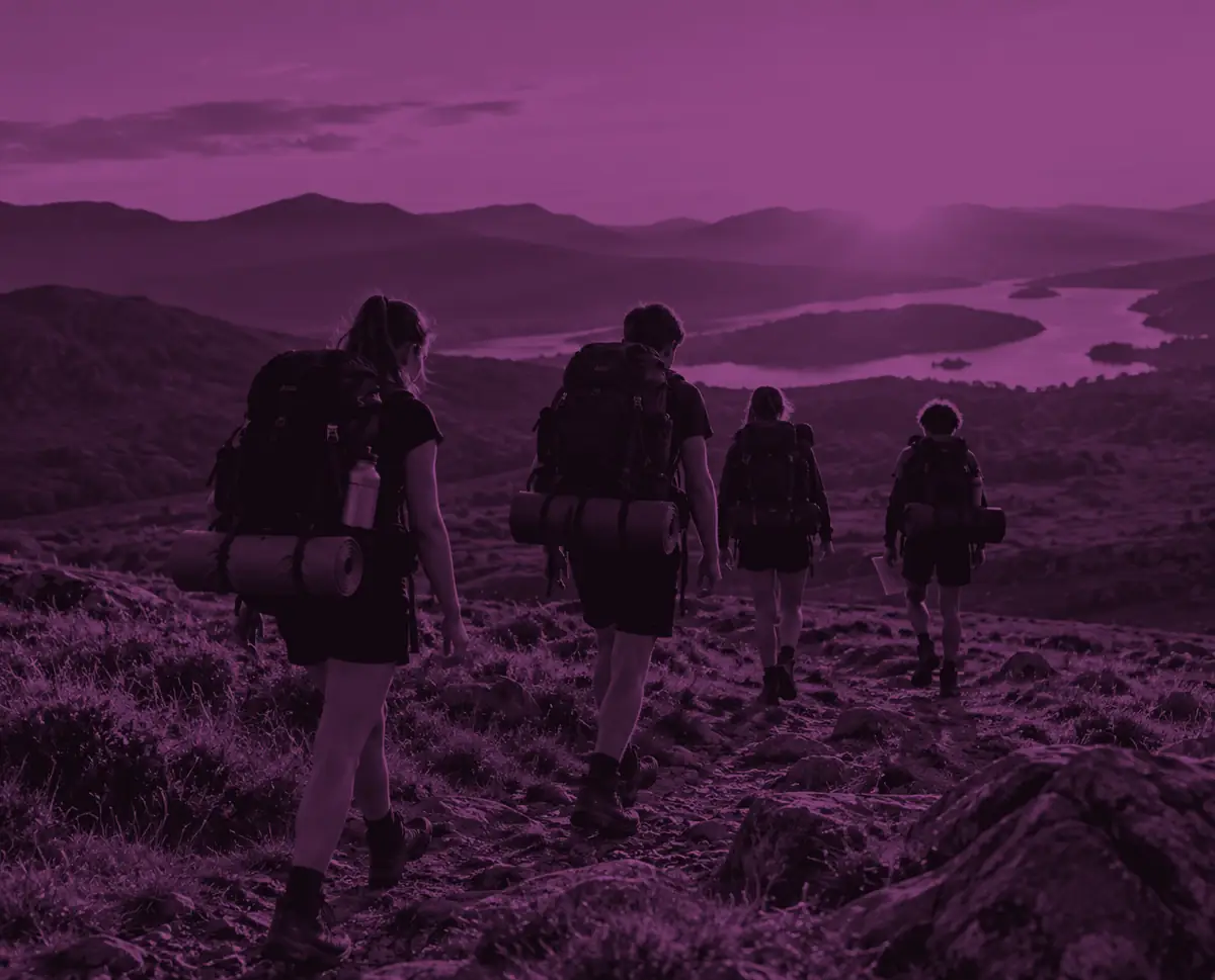 A Gold group walking away across open moorland at sunset with a lake far below, washed in purple